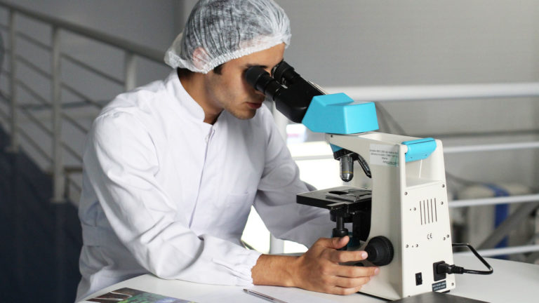 Lääketutkimuksen ammattilainen katsoo mikroskooppiin.